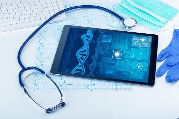 tablet with DNA on screen sitting on desk with cardiac EKG, masks, medical gloves, and stethoscope