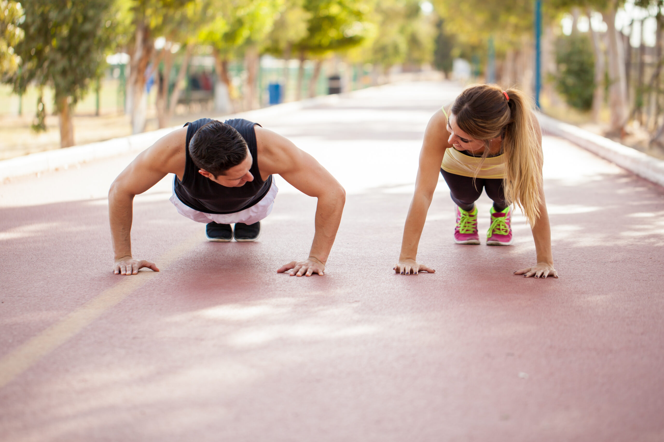 man and woman working out, doing push ups outside on path