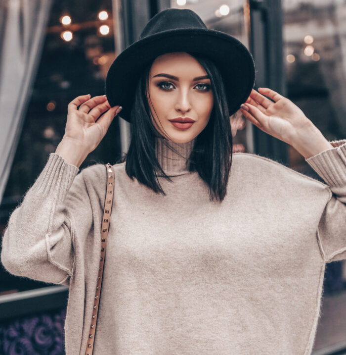 fashion outdoor photo of young pretty woman with short dark hair in elegant outfit and black hat walking on the street